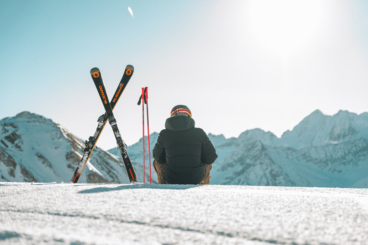 Sciatore seduto sulla neve accanto a sci incrociati, con le montagne innevate sullo sfondo